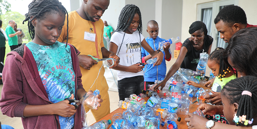 An Ibadan Waste Museum team member, teaching the children how to turn waste bottles into fashionable wear.